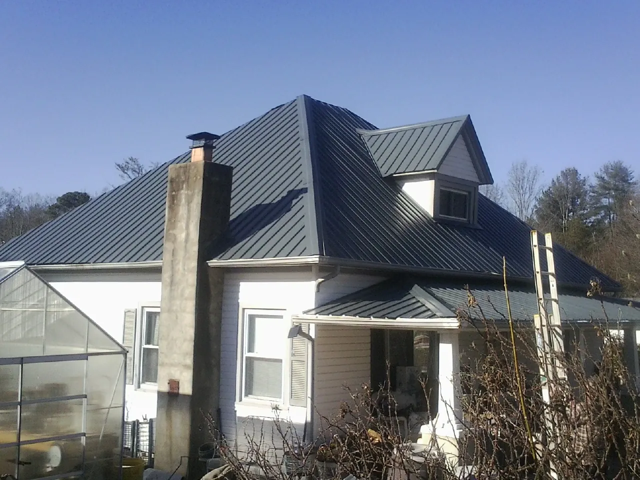 Dark blue standing seam metal roof on a white farmhouse with dormer — Slate & Tile Roof Repair by Roofing Brothers in North Powder