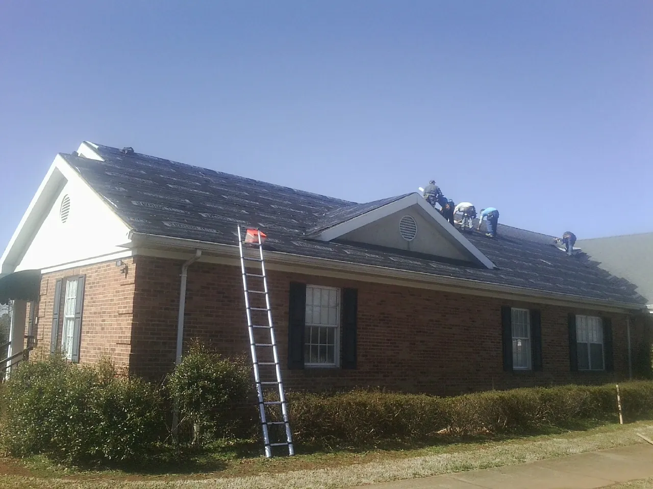 Crew tearing shingles off a brick ranch roof with a ladder set — Metal Roof Repair work by our crew in North Powder