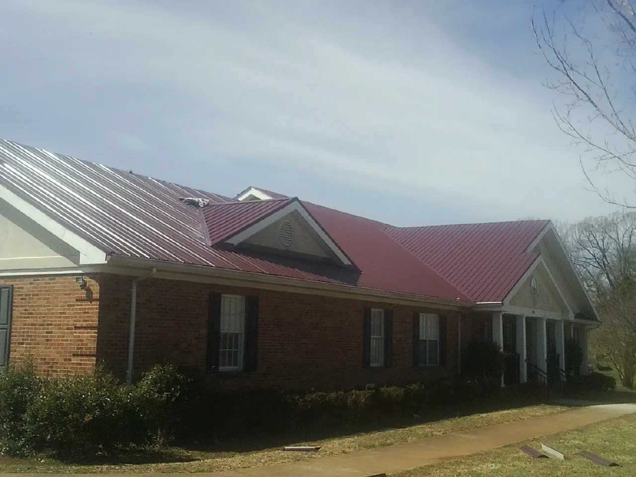 Red metal roof with gabled entries on a long brick building, from a Hail Damage Roof Repair job in North Powder