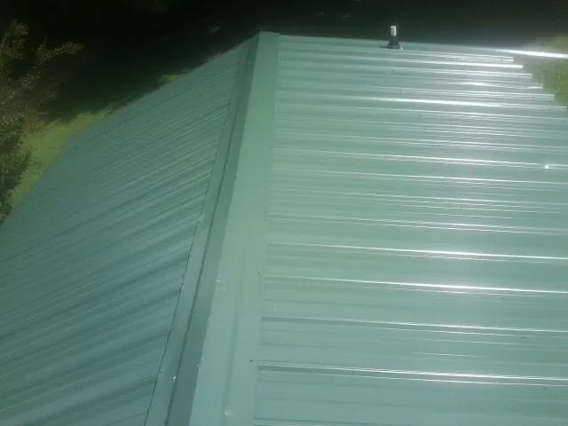 New green metal panels meeting at the ridge of a roof — Flat Roof Repair work by our crew in North Powder