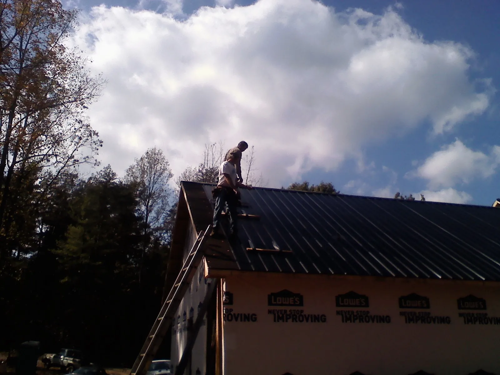 Roofer fastening dark metal panels high against a cloudy sky, from a Roof Inspection job in North Powder