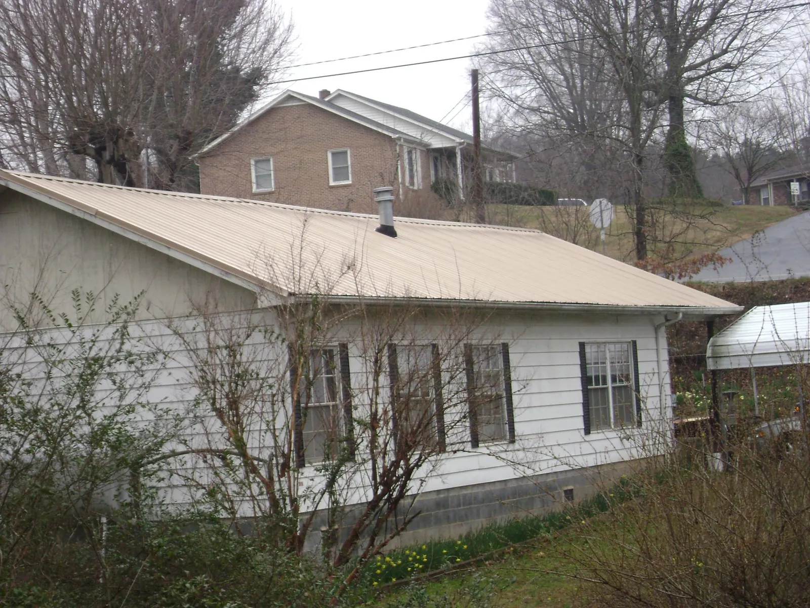 Tan metal roof on a white sided house set into a hillside — Commercial Roofing by Roofing Brothers in North Powder